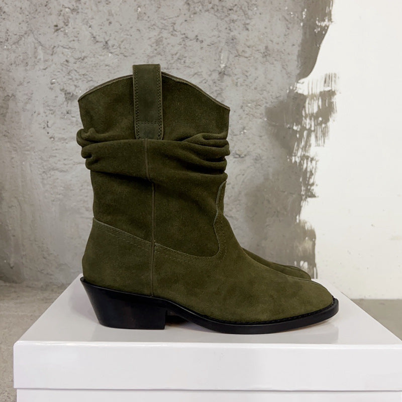 Green suede boot on a white pedestal against a textured gray wall.