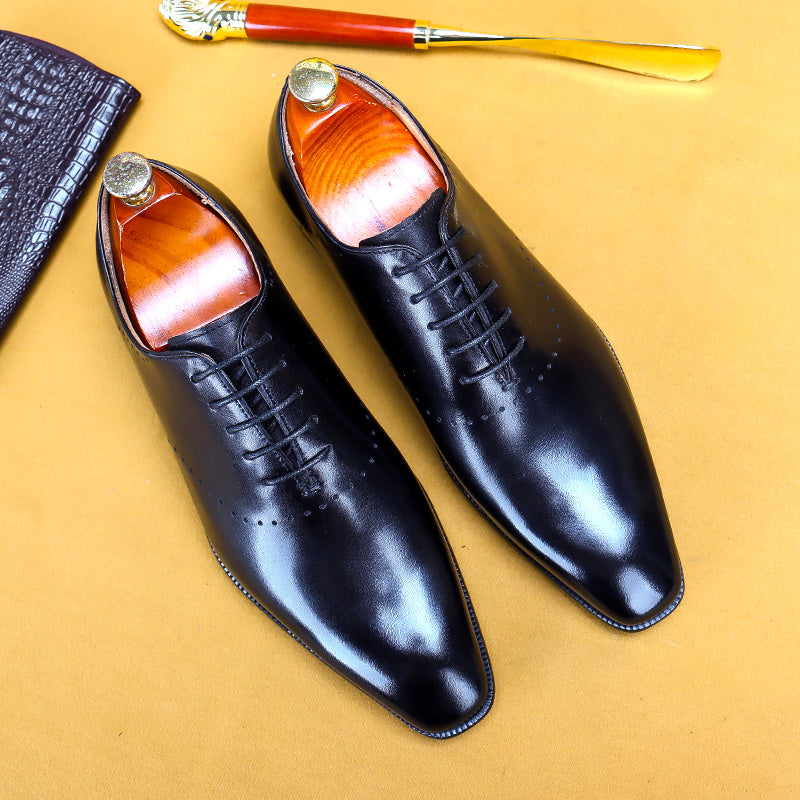 Pair of black dress shoes with brown soles on a yellow background