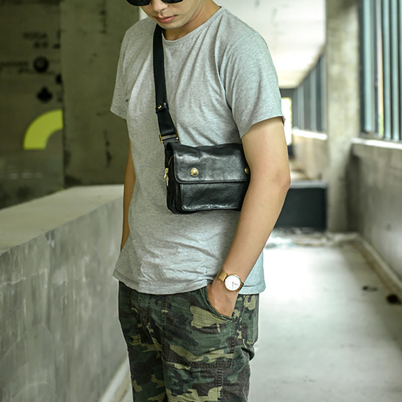Person wearing a gray t-shirt, black crossbody bag, and camouflage pants in an indoor setting.