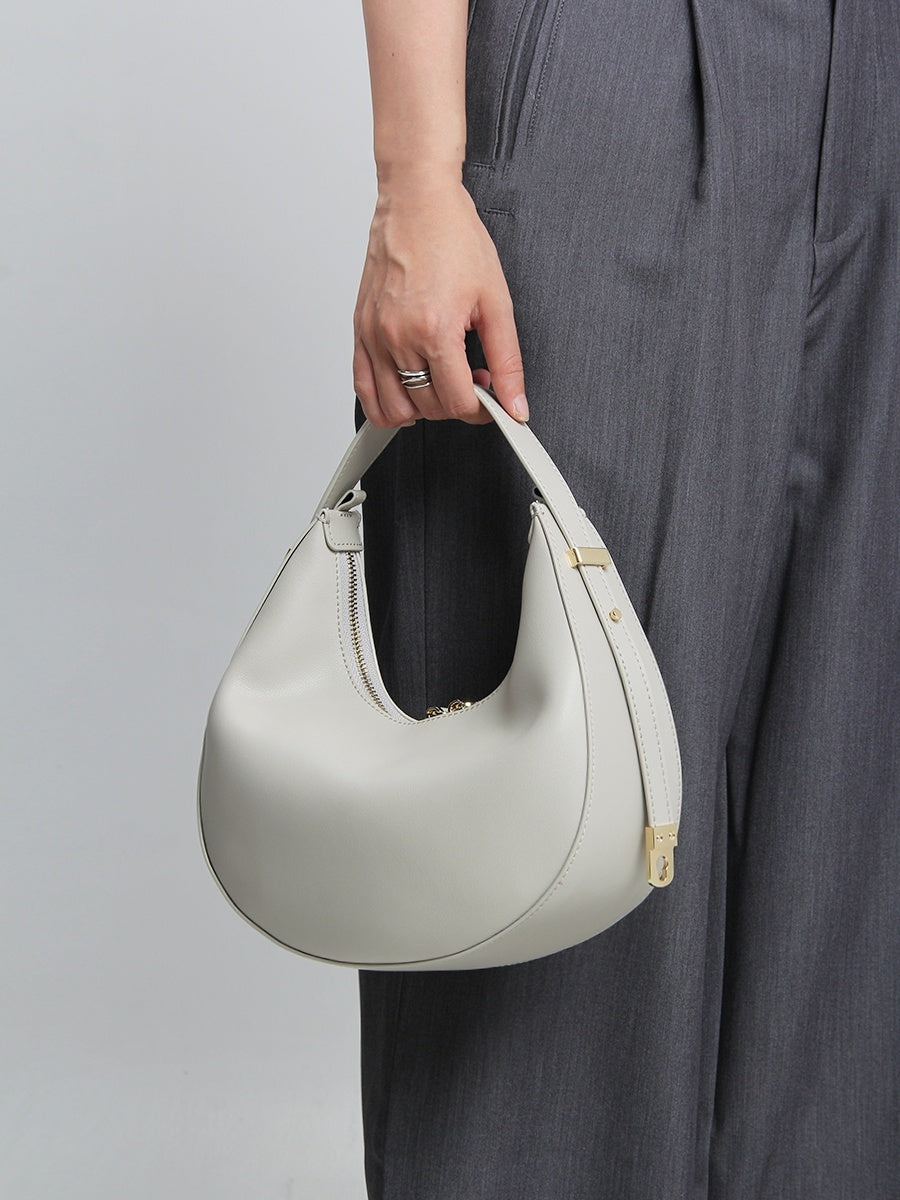 Person holding a light gray handbag against a plain background
