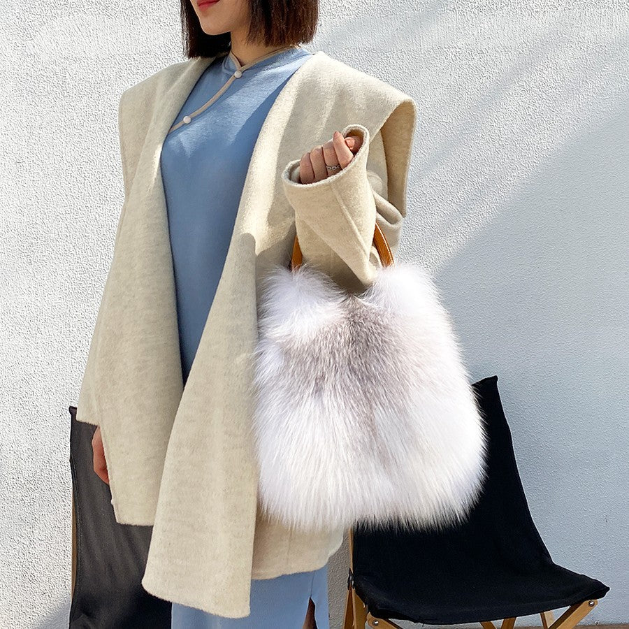 Person wearing a beige coat holding a white fluffy bag against a light gray background