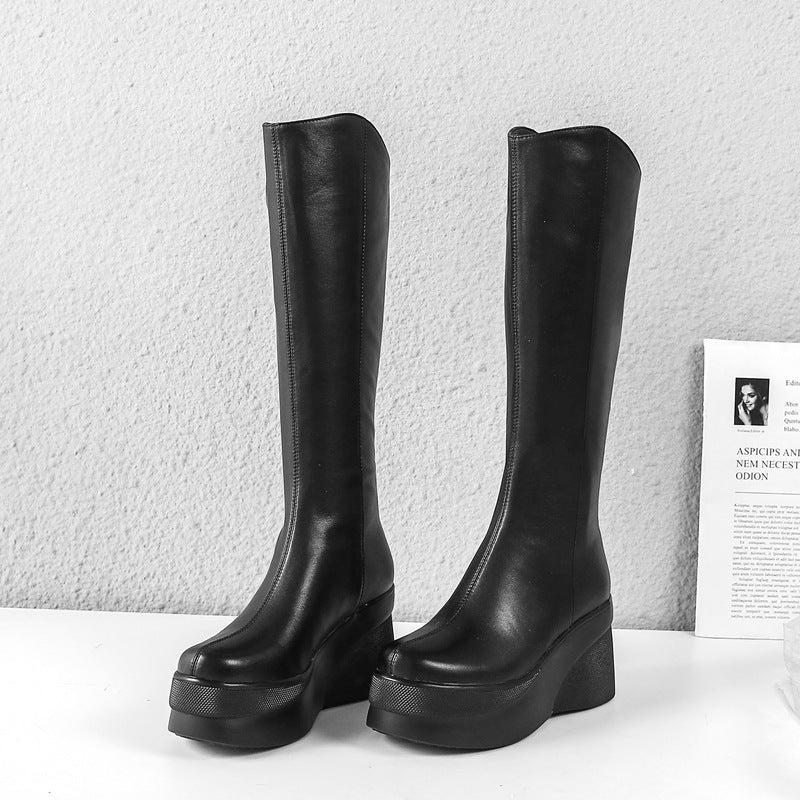 Black knee-high platform boots on a white surface with a light gray background