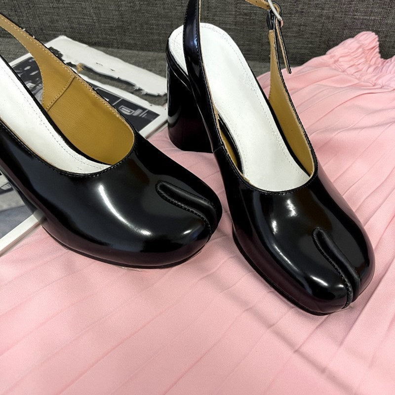 Black high-heeled shoes with a unique toe design on a pink surface.
