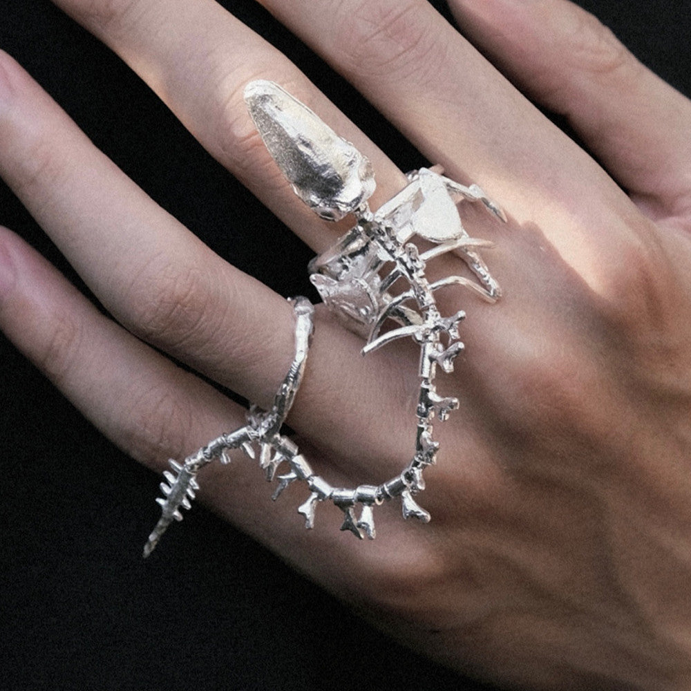 Silver skeleton hand ring on a hand against a dark background