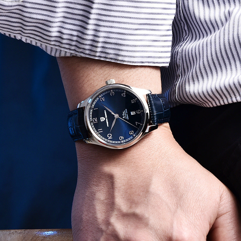 Person wearing a watch with a blue strap and dark face, set against a blurred background.