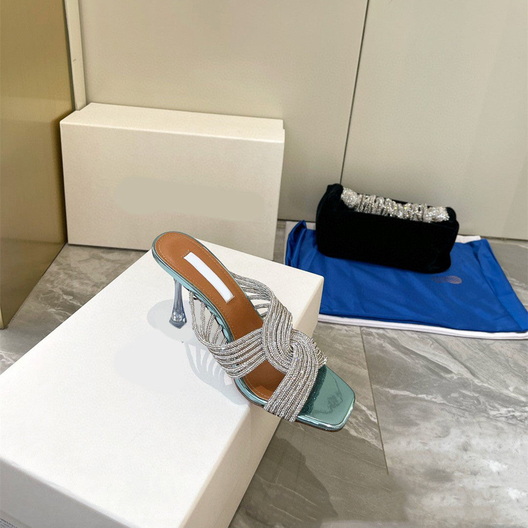 High-heeled sandal with decorative straps on a white surface, with a black clutch and blue mat in the background.