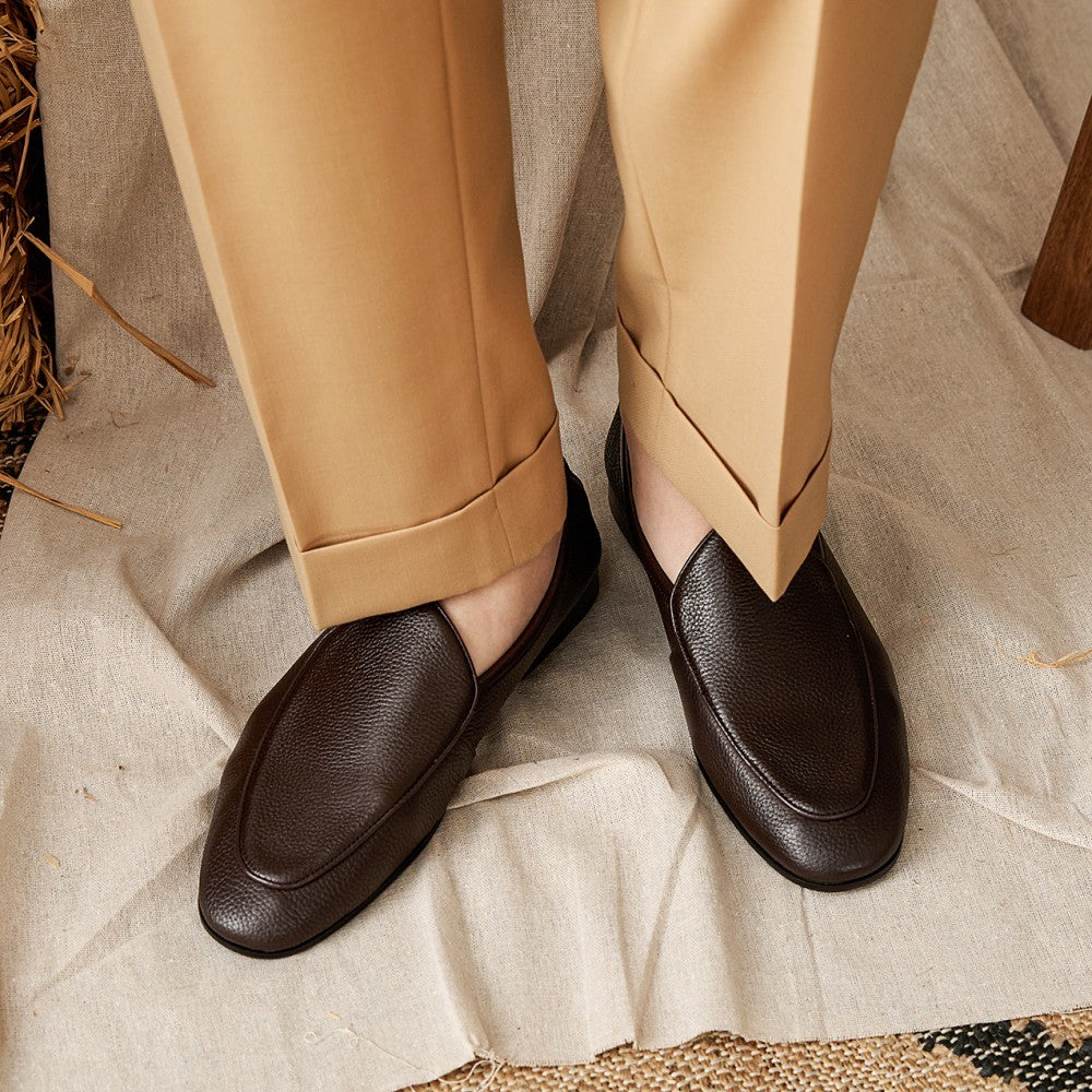 Brown leather loafers worn with beige pants on a textured surface