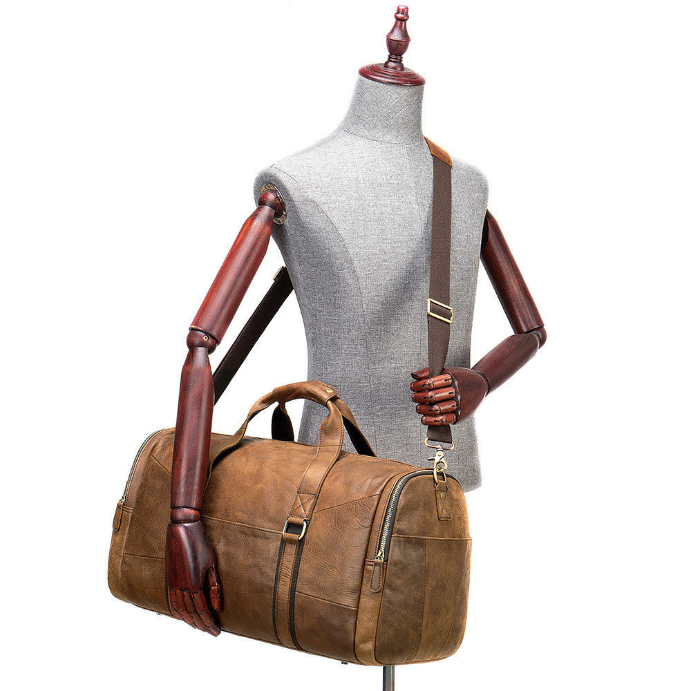 Brown leather duffel bag on a mannequin with wooden arms and hands against a white background