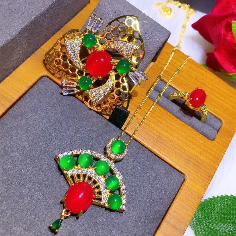 Gold jewelry set with red and green gemstones on a wooden surface
