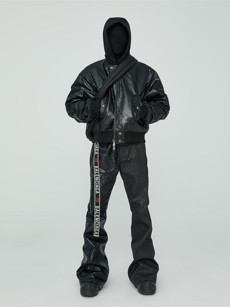 Person wearing a black leather jacket and pants with a white stripe on a light gray background