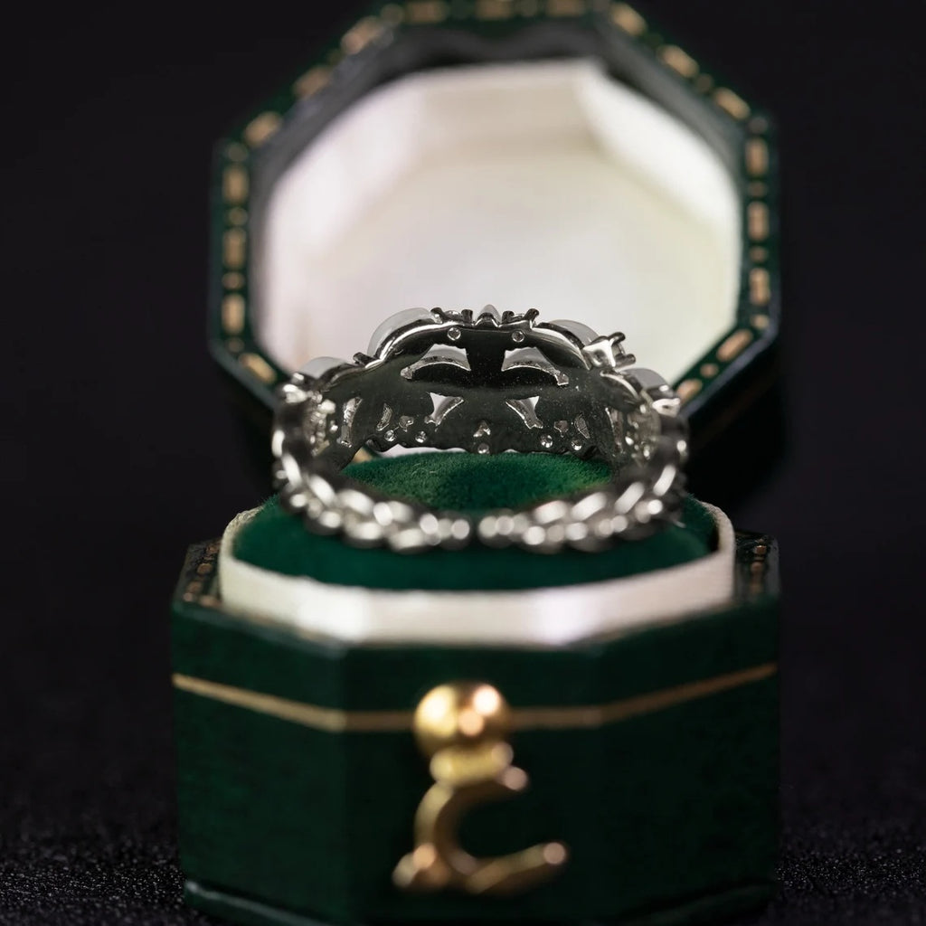 Silver ring with intricate design in a green jewelry box on a dark background