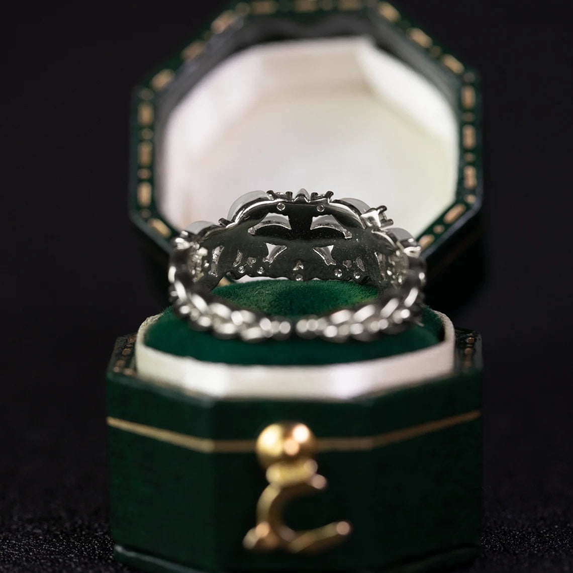 Silver ring with intricate design in a green jewelry box on a dark background