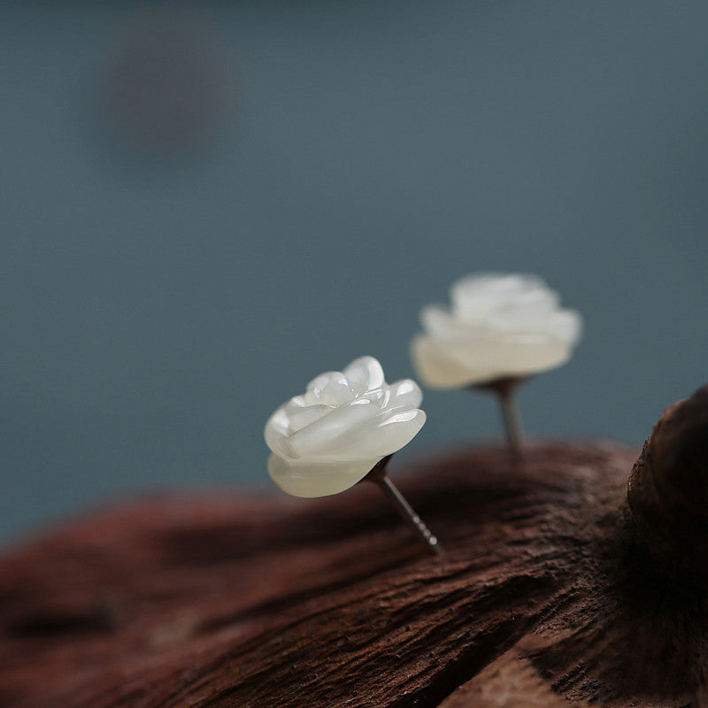 Pair of white flower-shaped earrings on a wooden surface with a blurred background