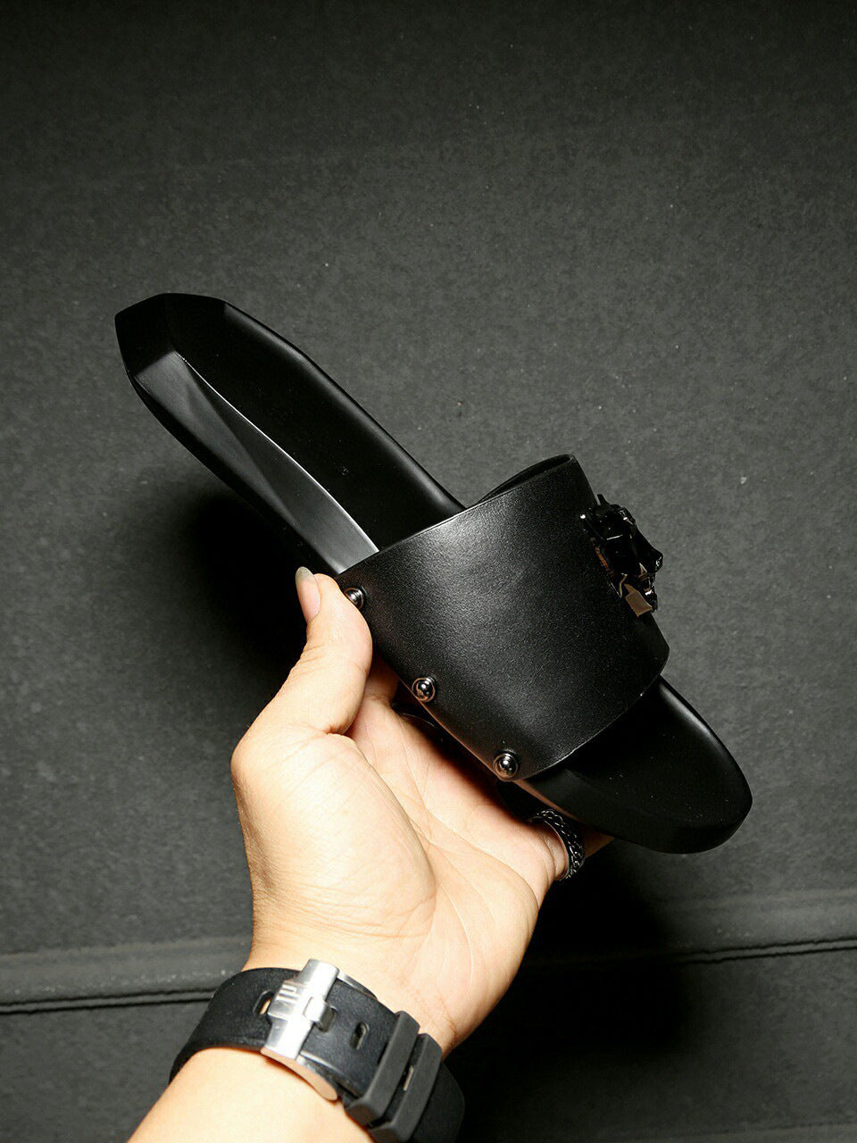 Black sandal held by a hand against a dark background
