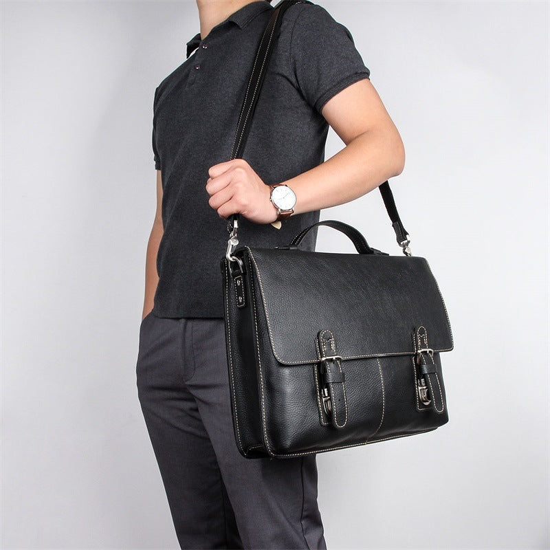 Person holding a black leather satchel bag against a plain background