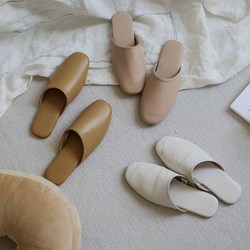 Pair of beige and white slippers on a light-colored surface with a neutral background.