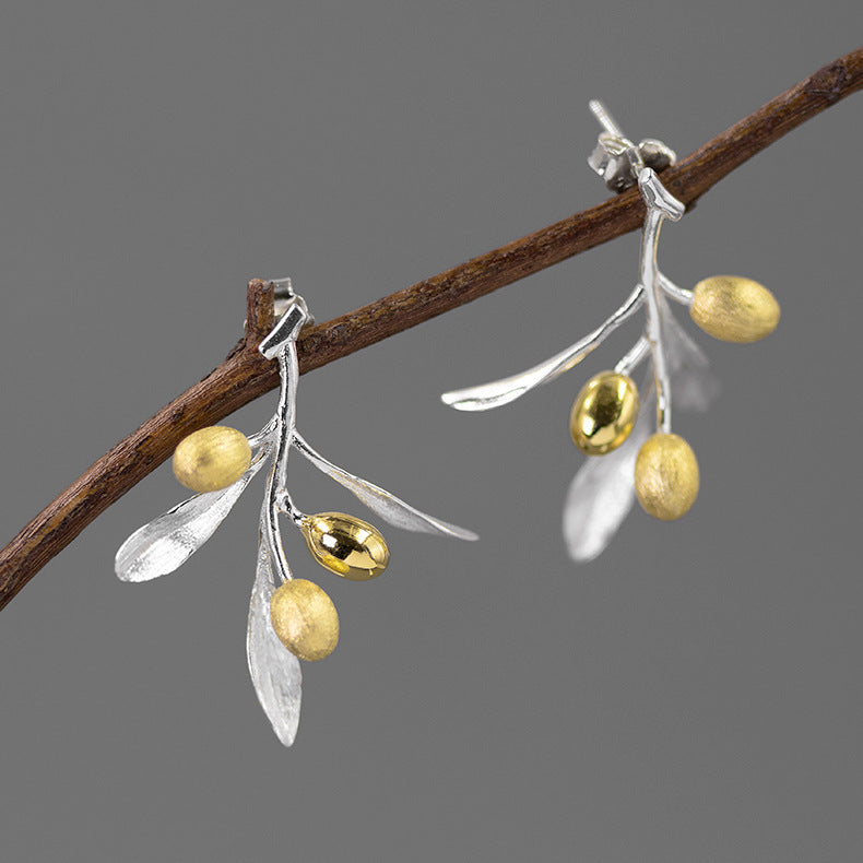Pair of earrings with gold and silver leaves on a branch against a gray background