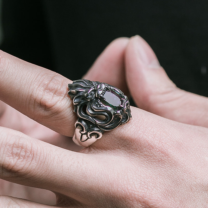 Silver ring with intricate design on a person's finger against a dark background