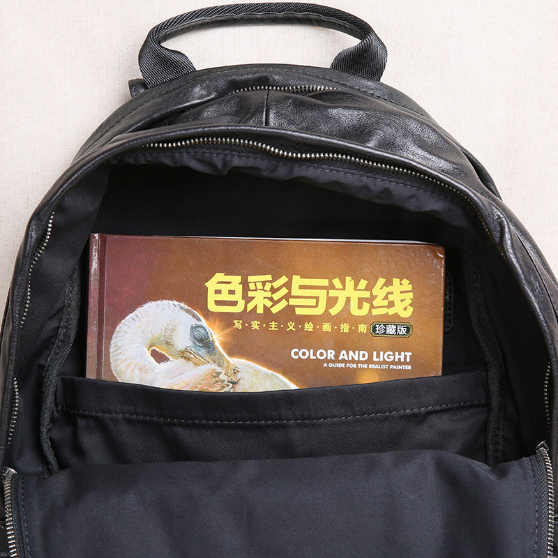 Black leather backpack with a book titled 'Color and Light' inside on a white background