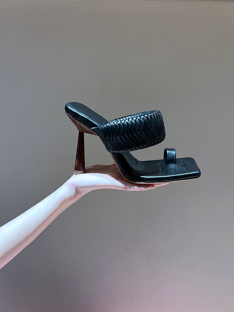 Black high-heeled shoe held in a hand against a plain background