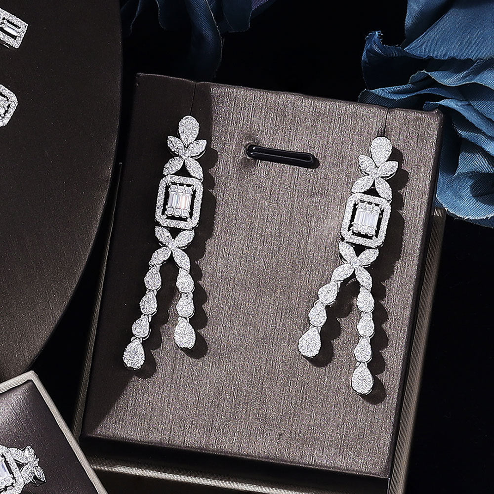 Pair of silver earrings on a gray jewelry display box with a dark background.