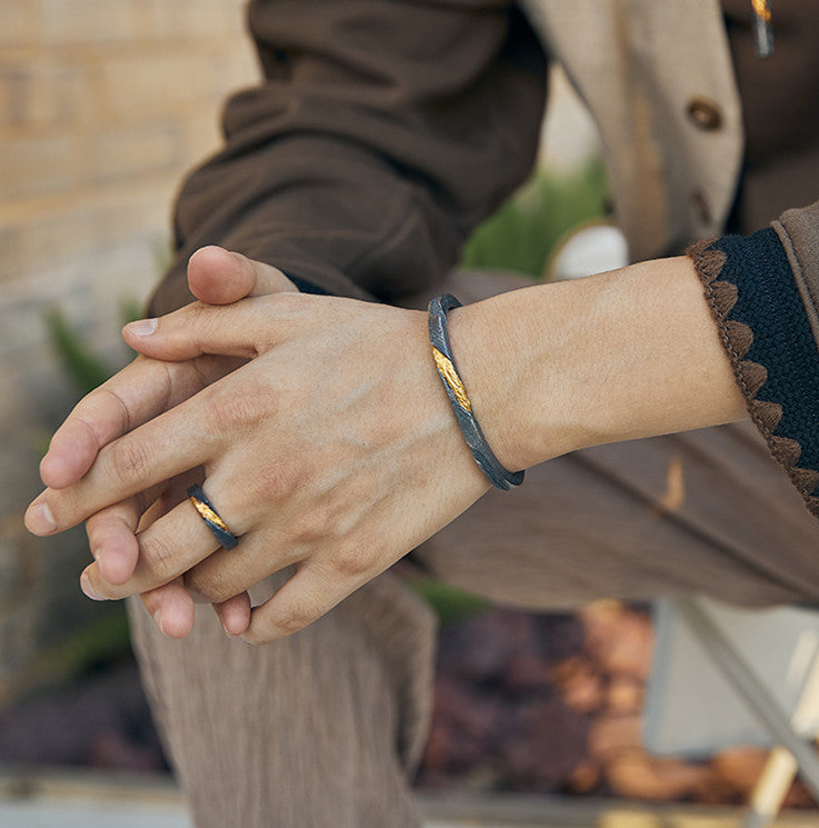 Close-up of two hands holding each other, wearing matching black bracelets with gold accents.
