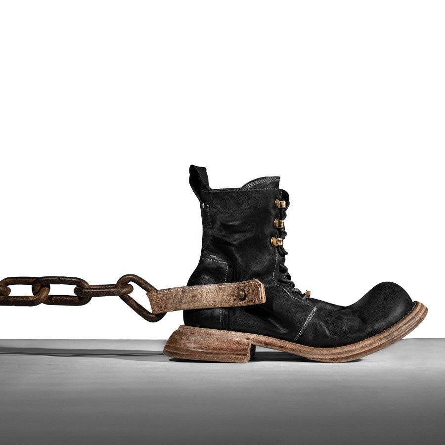 Black leather boot with gold accents and a chain on a white background