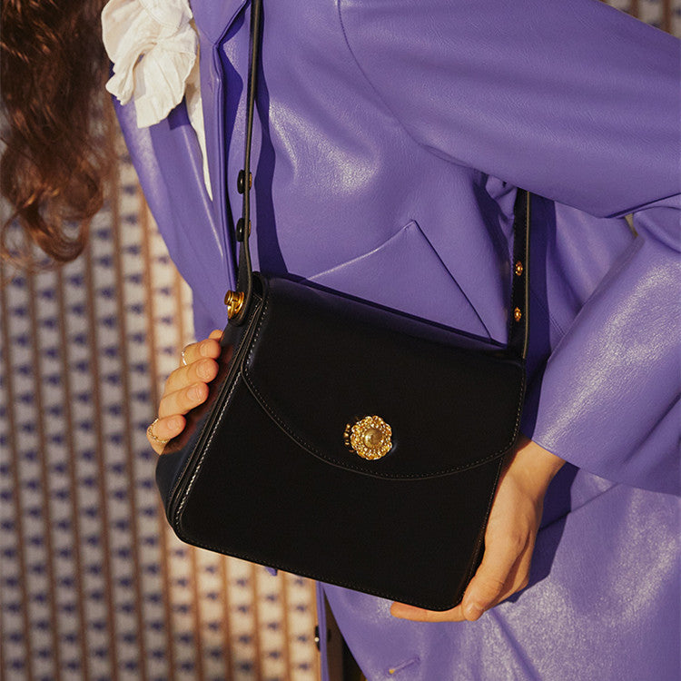 Person holding a black handbag with a gold emblem, wearing a purple outfit.