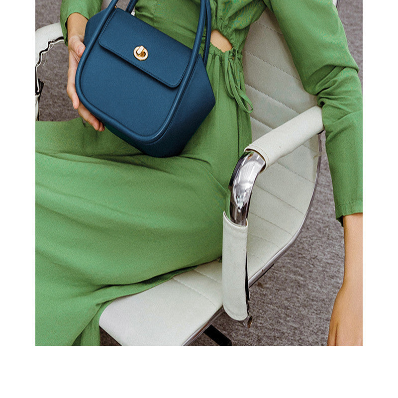 Person holding a blue handbag with a green outfit, sitting on a white chair.