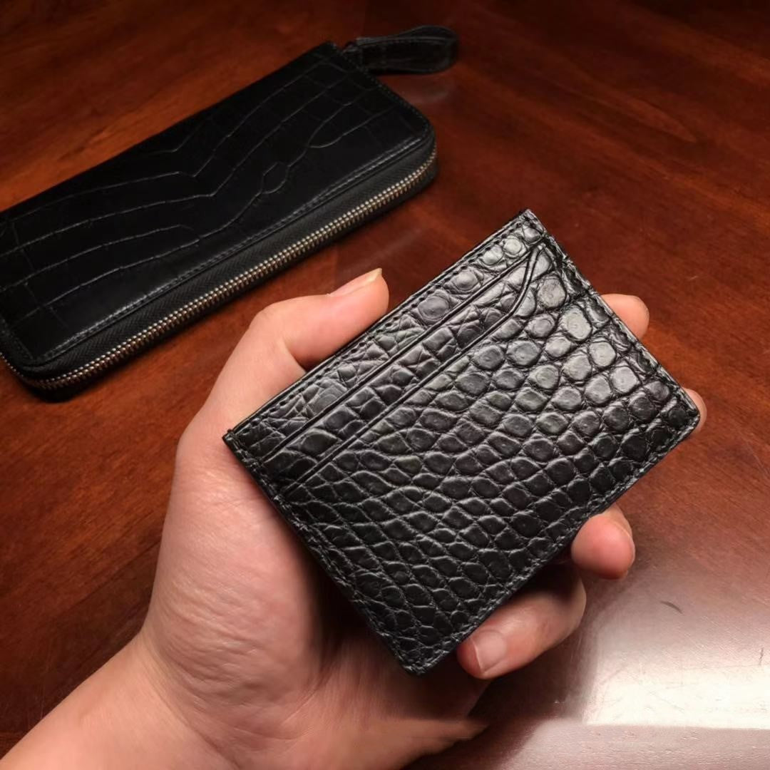 Black textured wallet held in a hand with another similar wallet in the background on a wooden surface.