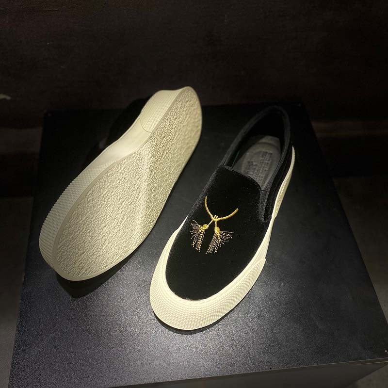Black slip-on shoes with gold embroidery on a dark surface