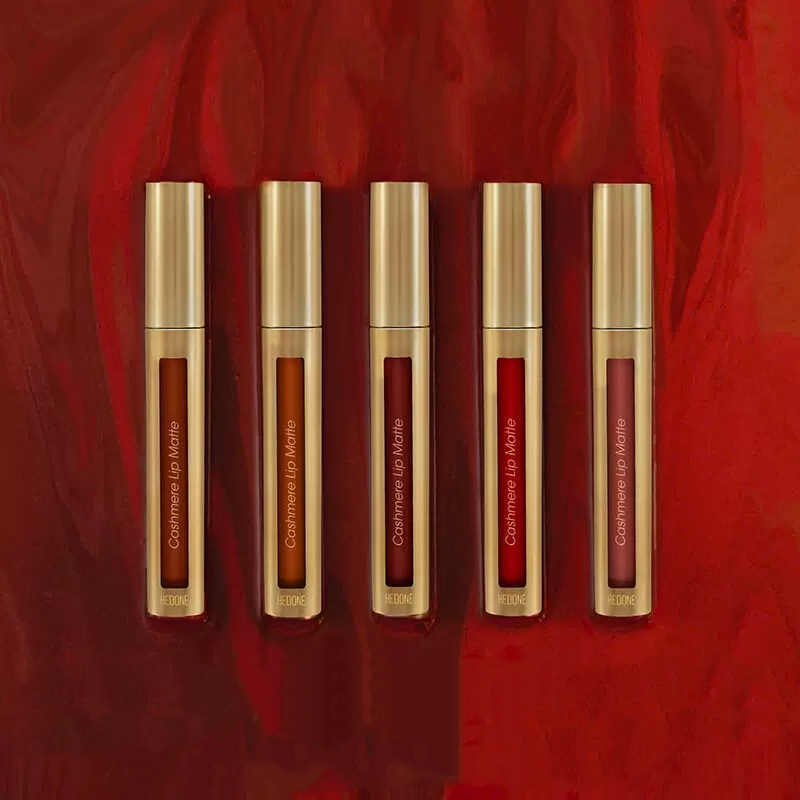 Five gold lip gloss tubes with red shades on a red background