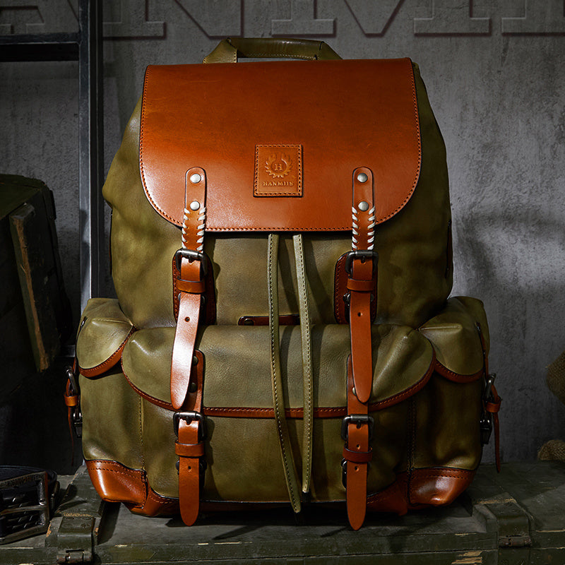 Green backpack with brown leather straps and accents on a textured surface.