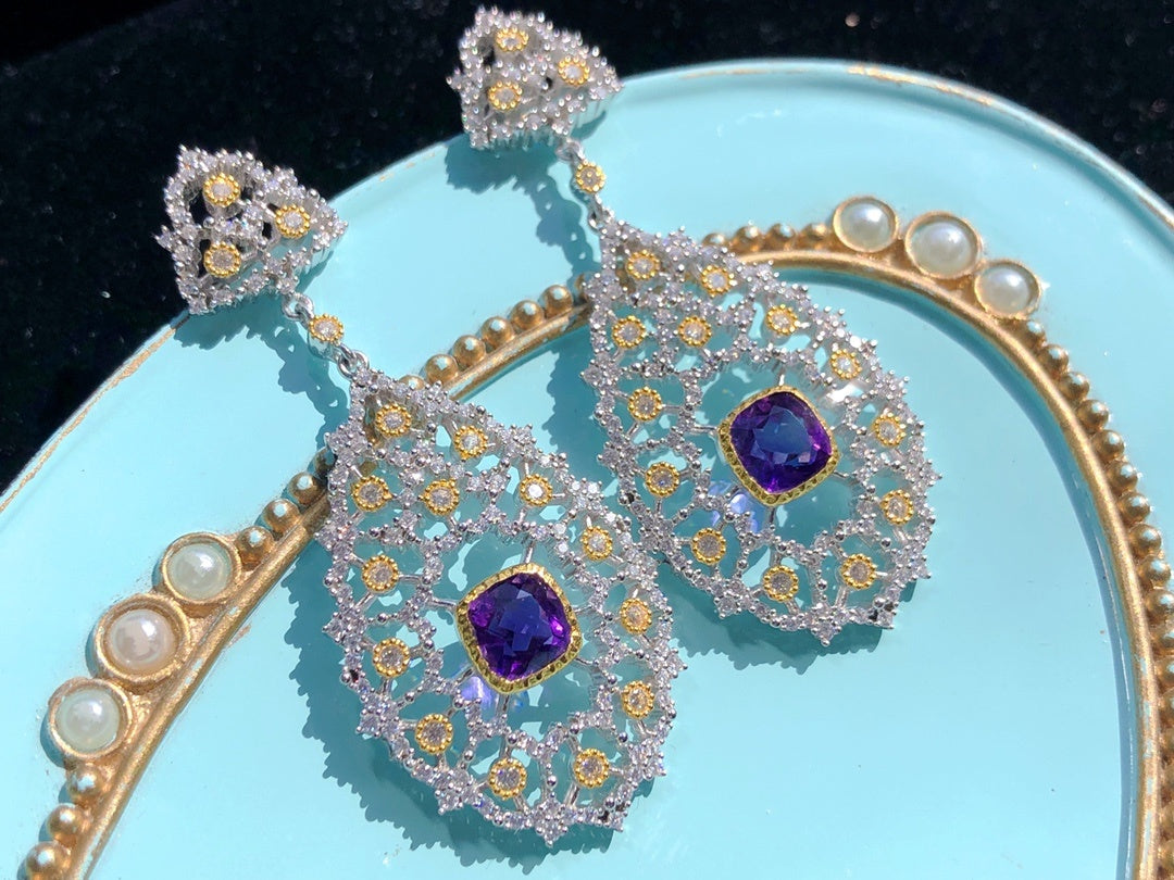 Ornate earrings with purple gemstones on a light blue plate