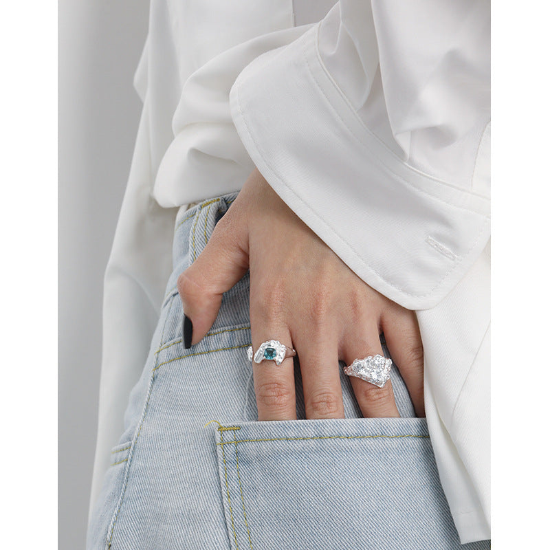 Hand wearing two rings with gemstones, one on each finger, against a neutral background.