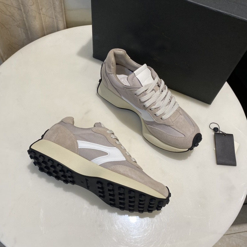 Pair of beige sneakers on a white surface with a black box in the background.