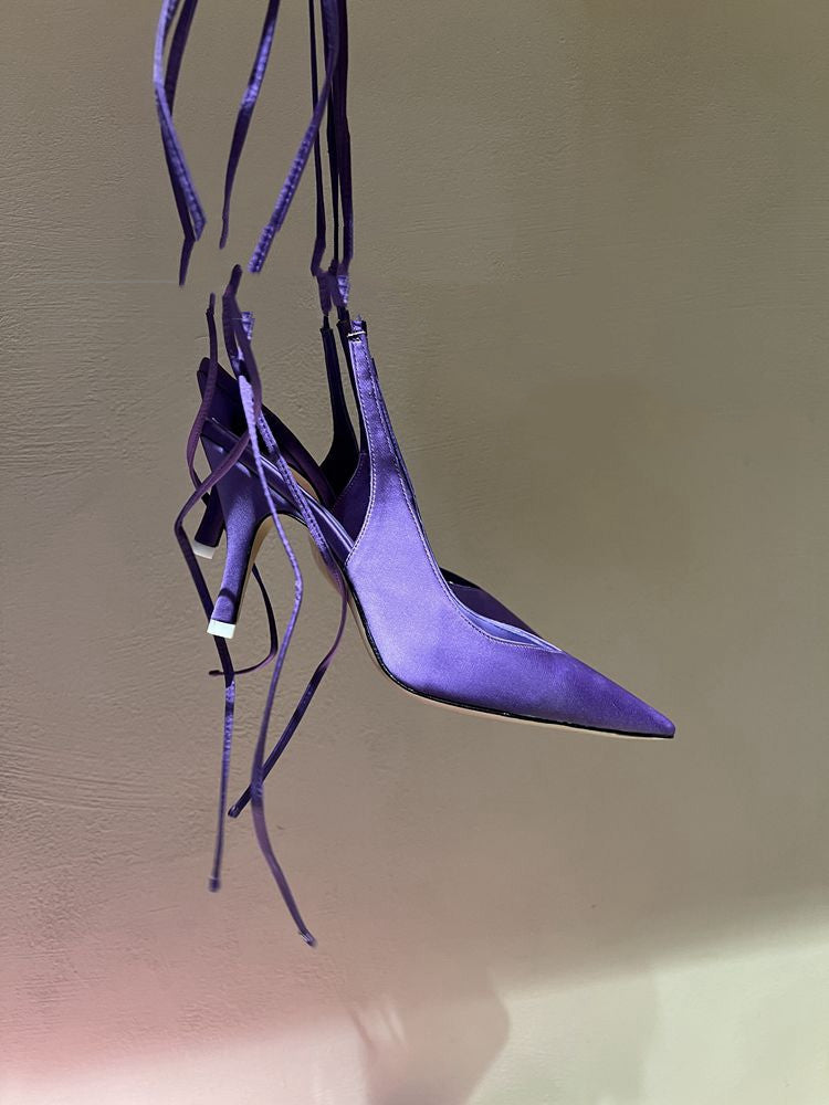 Purple high-heeled shoe with thin straps on a reflective surface