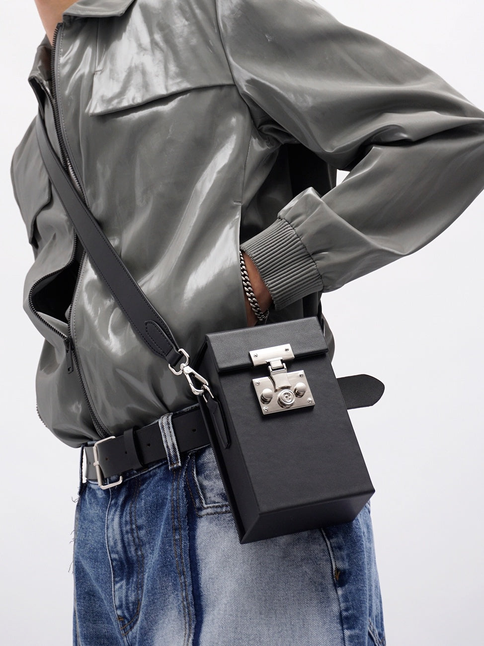Person wearing a gray jacket with a black crossbody bag on a white background