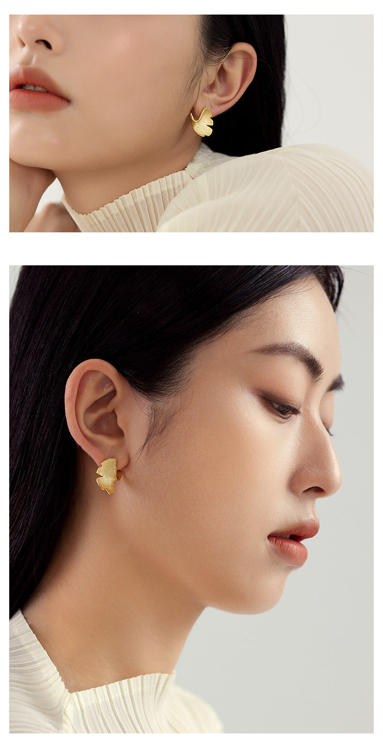 Close-up of a woman wearing gold earrings with a plain background
