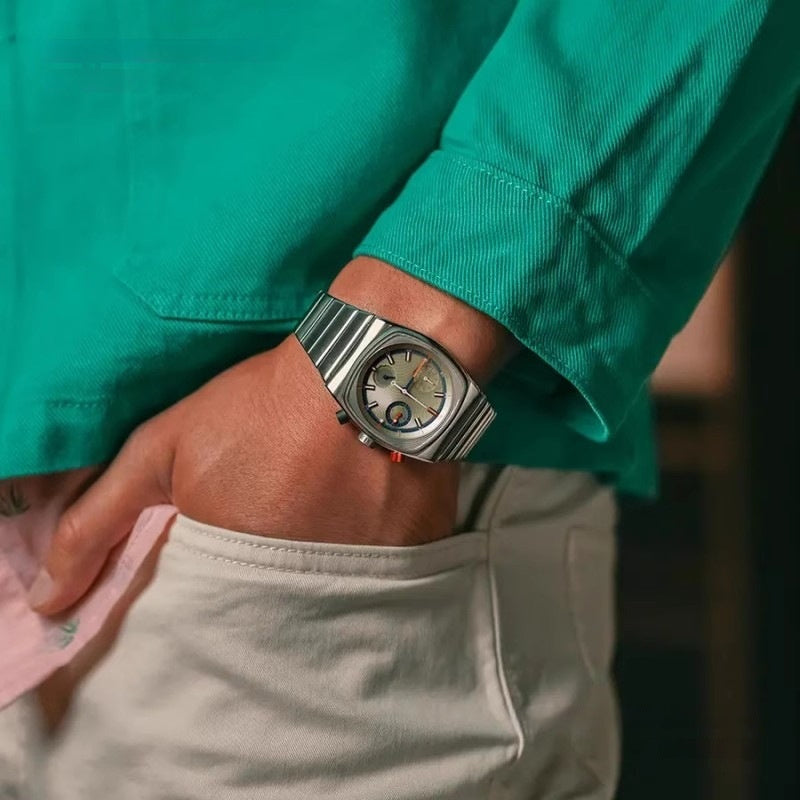 Person wearing a silver wristwatch with a green shirt and light-colored pants.
