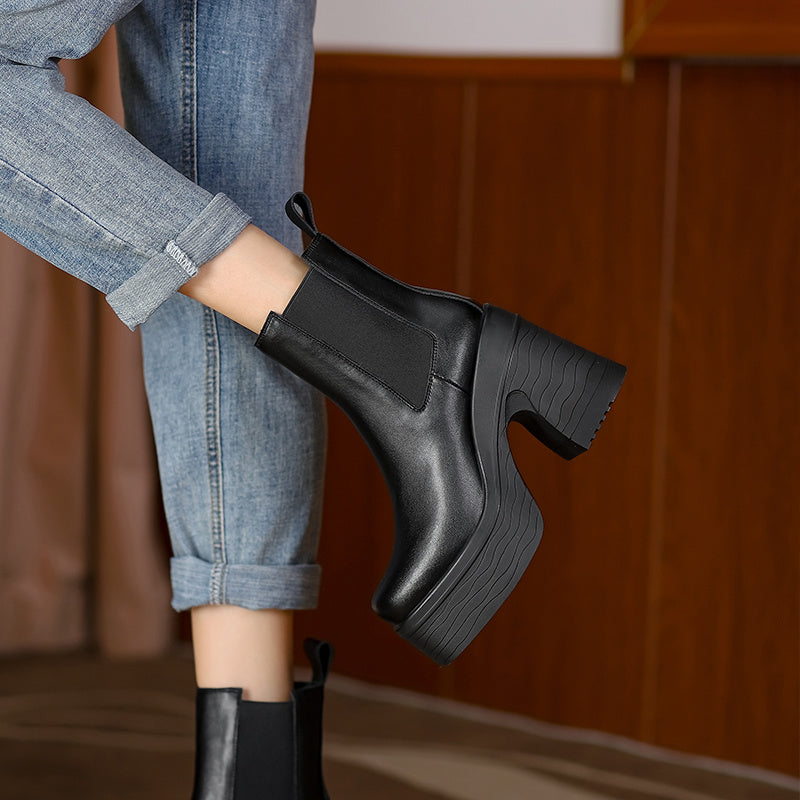 Black leather boot worn with rolled-up jeans against a wooden background