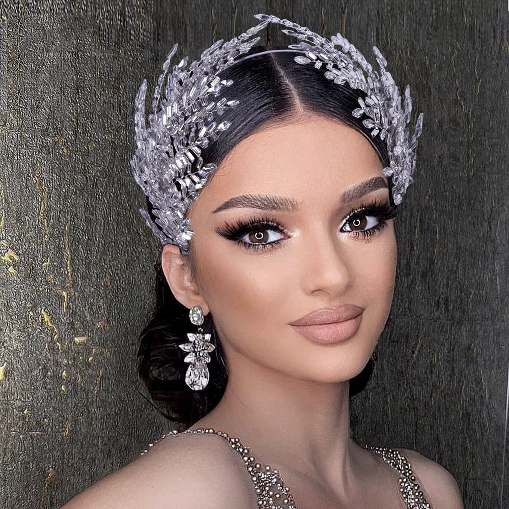 Woman wearing a decorative silver headpiece and earrings against a dark background