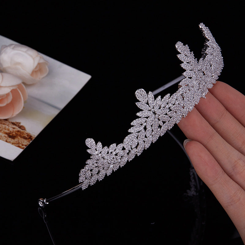 Silver decorative headband held by a hand with a blurred background