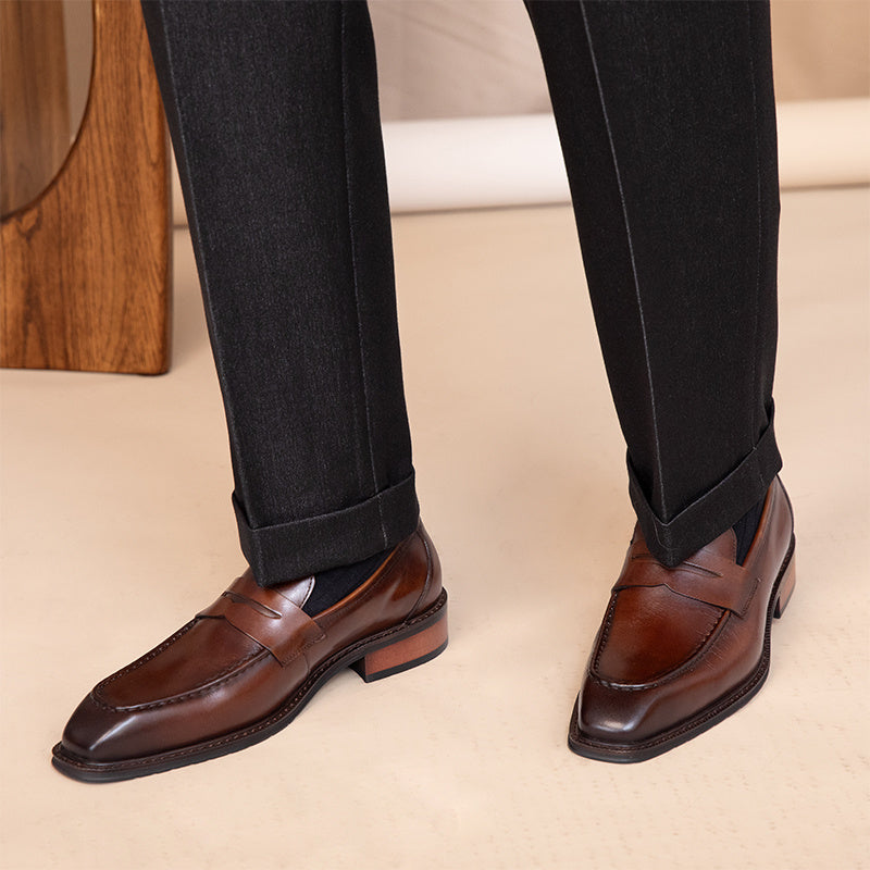 Brown dress shoes worn with black pants on a beige floor.