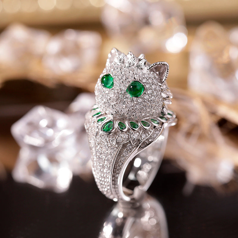Silver cat-shaped ring with green gemstones on a reflective surface