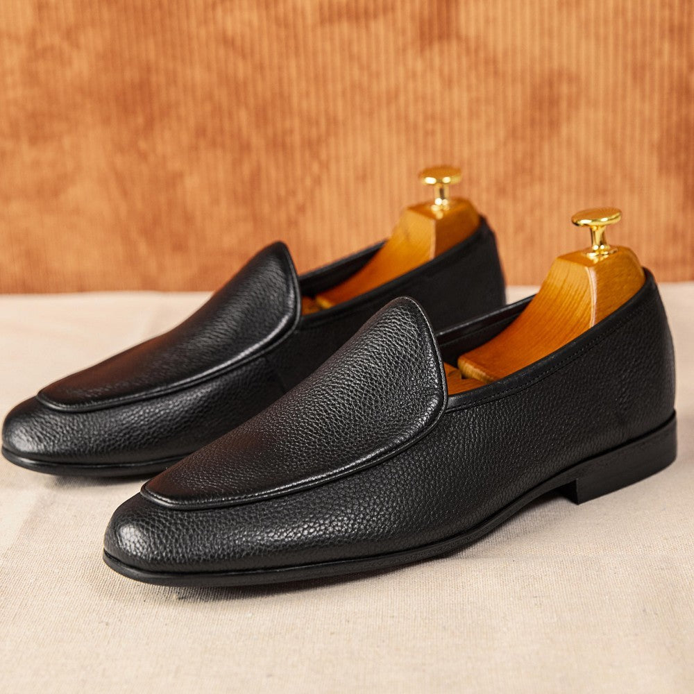 Pair of black leather loafers on a wooden stand with a beige background