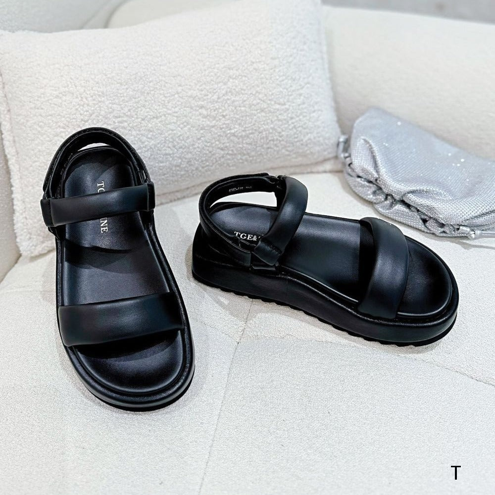 Black sandals on a light gray surface with a white pillow in the background