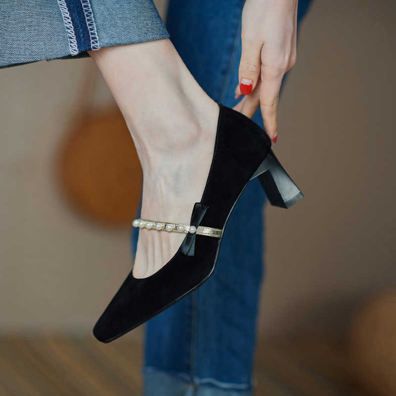 Black high-heeled shoes with pearl strap worn by a person in jeans.