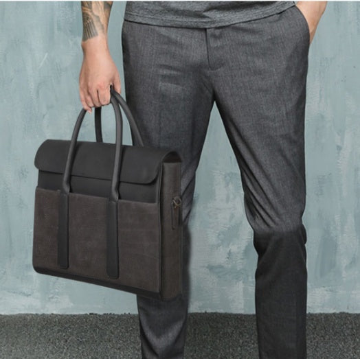 Person holding a dark gray briefcase against a textured light blue wall.