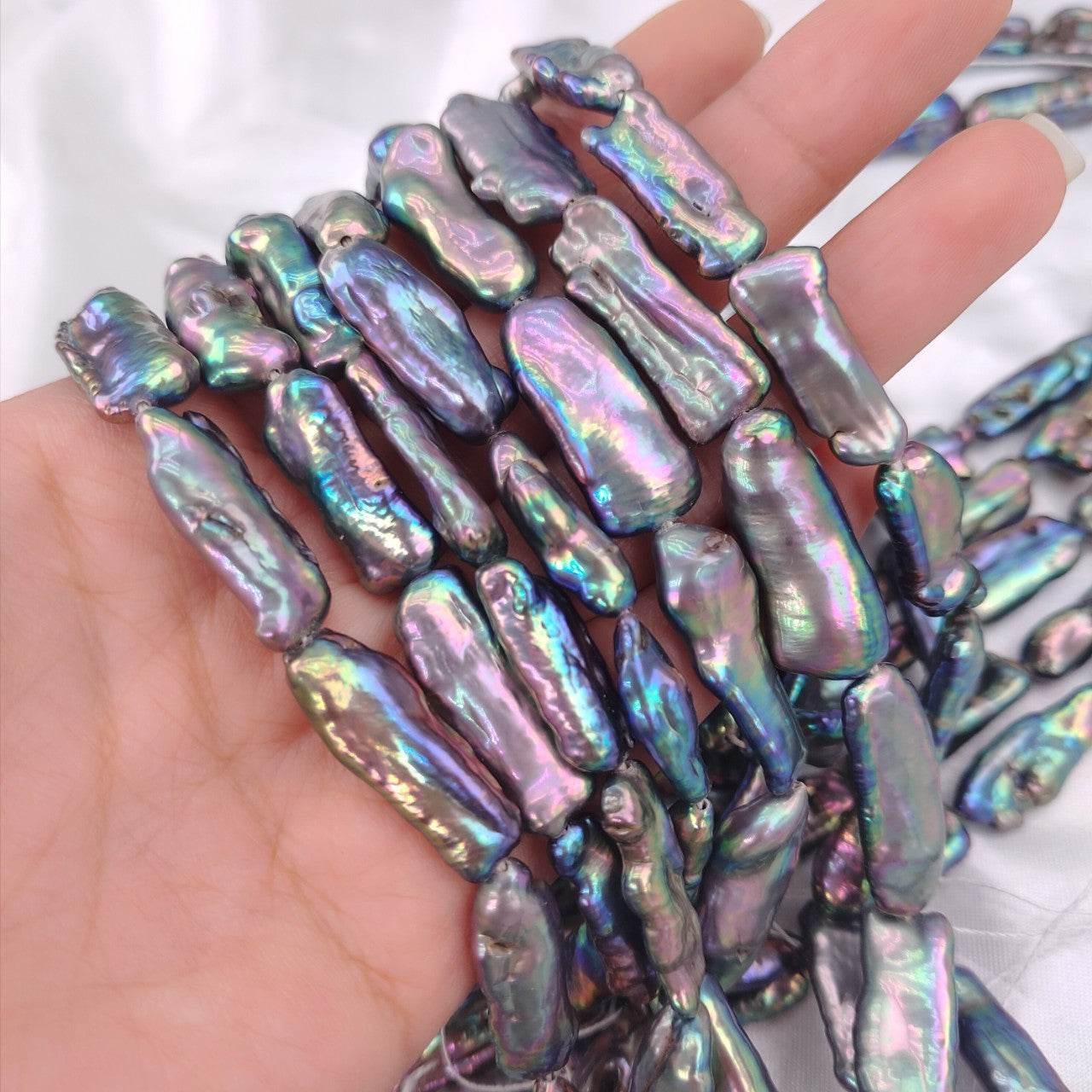 Iridescent baroque pearls held in a hand against a white background
